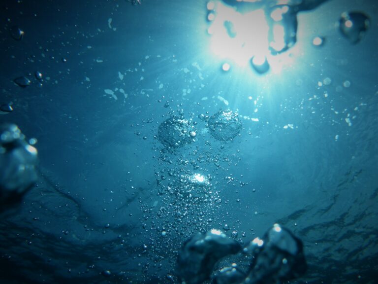 Underwater brilliant blue editorial image with bubbles and light streaming from top right corner.