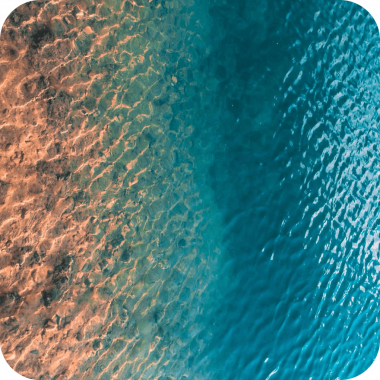 Aerial view of rippling water, turquoise blue water along a shallow, orange sandy coast